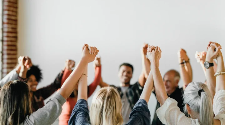 A diverse group of people standing in a circle, holding hands with their arms raised high in a gesture of unity and solidarity. A red graphic overlay on the left reads 'FROM AWARENESS TO ACTION' followed by the hashtag '#MENTALHEALTHMATTERS'.